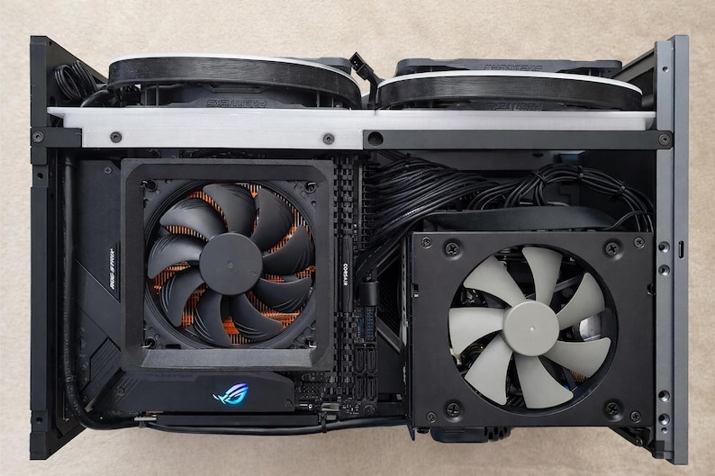 May include: A black computer case interior with multiple fans and components. The case features a large fan with black blades and copper-colored fins, along with other fans and wiring. The ROG logo is visible on a component.