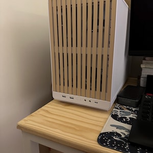 May include: A white computer case with a light brown wooden slat front panel. The case has multiple USB ports and audio jacks on the front. It sits on a light wood table.