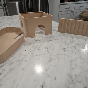 May include: A set of three light beige plastic components for a small animal habitat, including a rectangular tray, a square hideout with an arched entrance and a circular side opening, and a separate ramp piece with a textured, ribbed surface.