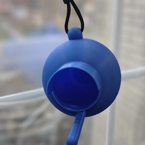 May include: A blue, spherical, 3D-printed plastic object with a circular opening on the front, a small handle extending downward, and a loop at the top attached to a black cord. The surface has a matte texture with visible horizontal print lines.