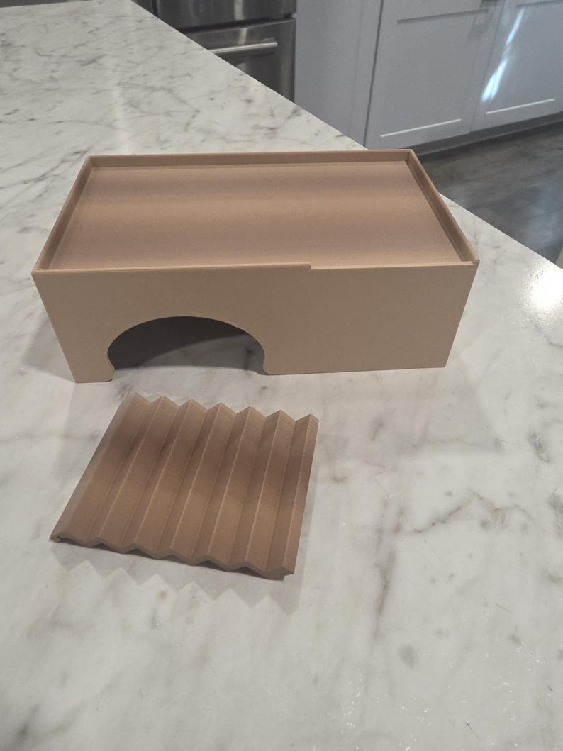 Puede incluir: Un recinto rectangular de color beige claro con una &uacute;nica abertura arqueada en la parte frontal y una pieza cuadrada separada a juego, de color beige claro, con una serie de crestas paralelas en zigzag en su superficie superior.