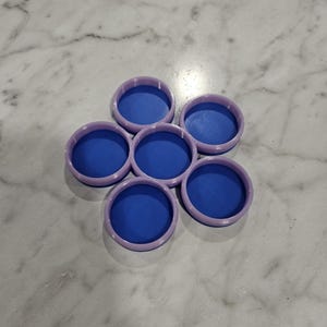 May include: A set of six blue and purple round coasters. The coasters are arranged in a flower shape.
