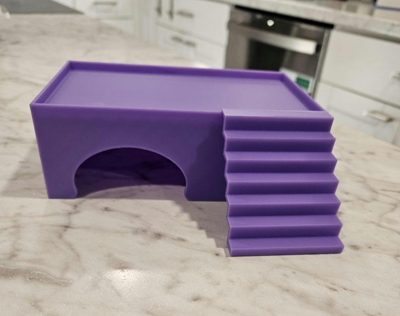 Puede incluir: Un escondite para mascotas de color morado s&oacute;lido que presenta una plataforma superior rectangular, una entrada en arco semicircular en la parte frontal y un conjunto de escaleras integradas que conducen al techo plano, hecho de material liso y mate.