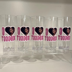 Pu&ograve; includere: Cinque bicchieri alti e trasparenti, ognuno caratterizzato da un design grafico con un cuore rosa contenente il ritratto di una persona, con il testo rosa "I LOVE TOONK" stampato sotto il cuore. I bicchieri hanno una base testurizzata a bolle.