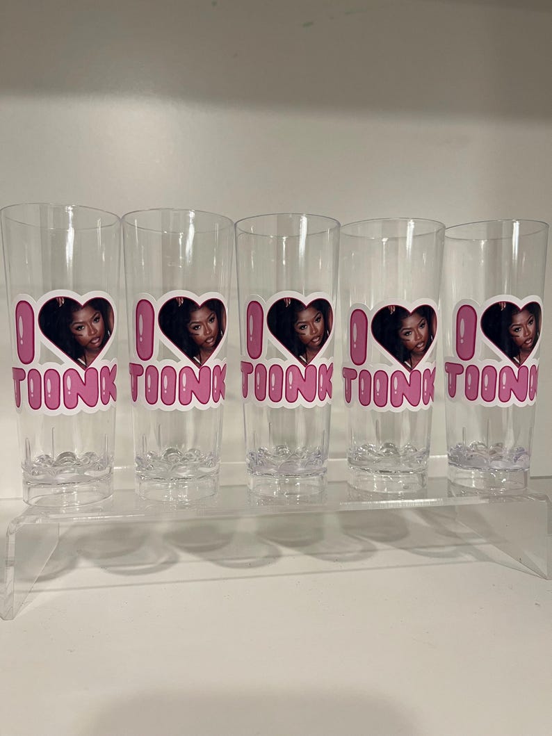Pu&ograve; includere: Cinque bicchieri alti e trasparenti, ognuno caratterizzato da un design grafico con un cuore rosa contenente il ritratto di una persona, con il testo rosa "I LOVE TOONK" stampato sotto il cuore. I bicchieri hanno una base testurizzata a bolle.