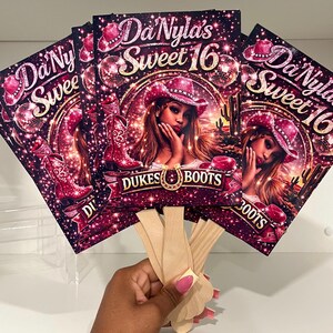 May include: A stack of decorative fans with a cowgirl theme. Each fan features a portrait of a woman wearing a pink cowboy hat, with the text "Da'Nyla's Sweet 16" and "Dukes Boots". The fans have wooden handles.