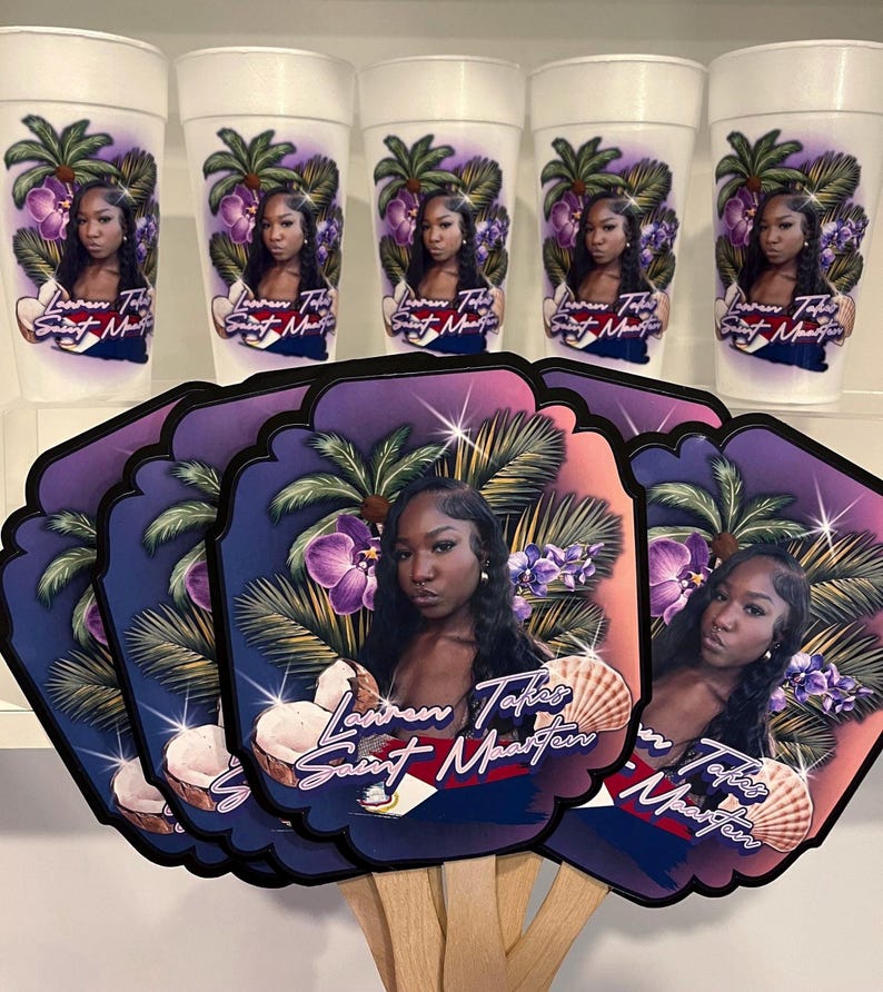 May include: A collection of personalized party favors, including white foam cups and decorative hand fans. The cups and fans feature a portrait of a woman, tropical imagery, and the text "Lauren Takes Saint Maarten."