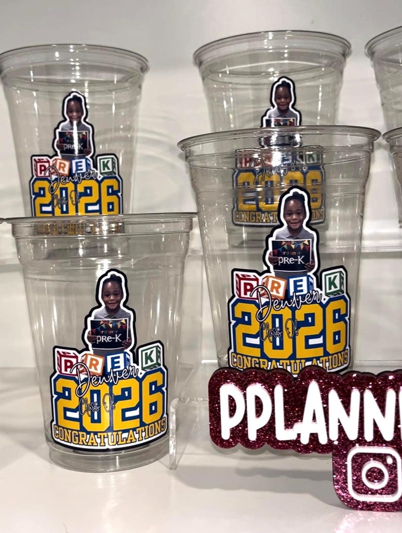 May include: Clear plastic cups featuring a graphic of a child holding a sign that reads pre-K, with colorful alphabet blocks, the text Denver Class of 2026, and the word CONGRATULATIONS in yellow and blue. A maroon glitter sign reads PPLANNER.