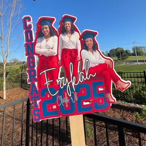 May include: A graduation yard sign featuring three images of a woman in a cap and gown, with the words "CONGRATS Erykah Class Of 2025" in red and blue. The woman is wearing a white top and red pants.