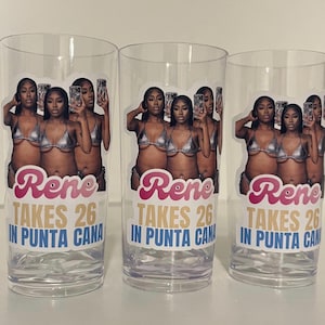 Pu&ograve; includere: Tre bicchieri in plastica trasparente con un adesivo fotografico di una persona in bikini argento che tiene in mano un telefono. Il testo recita "Rene TAKES 26 IN PUNTA CANA" in lettere rosa, oro e blu. Il design &egrave; ripetuto su ogni bicchiere.