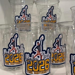 May include: A collection of clear plastic cups, each featuring a graphic decal with a person in a gymnastics pose, the name Hailey Clark, the year 2026, and the text Fisk University in blue and yellow lettering against a dark blue background.