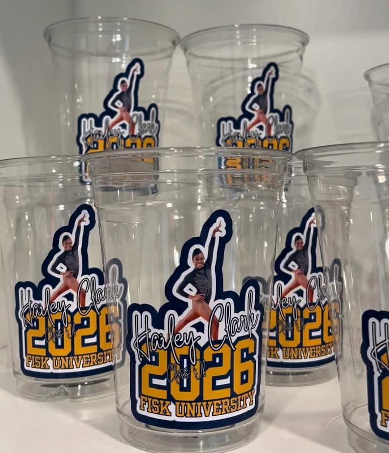 May include: A collection of clear plastic cups, each featuring a graphic decal with a person in a gymnastics pose, the name Hailey Clark, the year 2026, and the text Fisk University in blue and yellow lettering against a dark blue background.