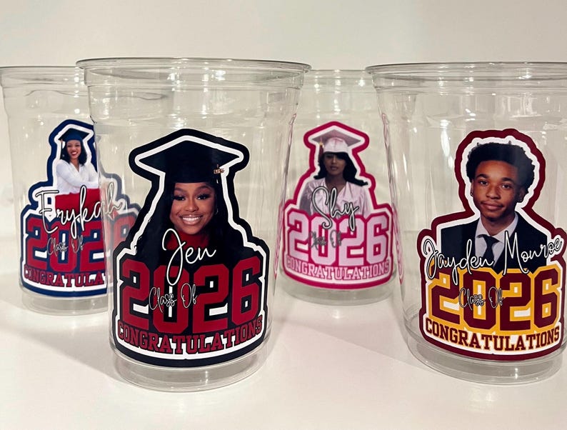 May include: Four clear plastic disposable cups featuring personalized graduation decals. Each cup displays a portrait of a graduate in a cap and gown, the name of the graduate, the year 2026, and the word CONGRATULATIONS in bold lettering.