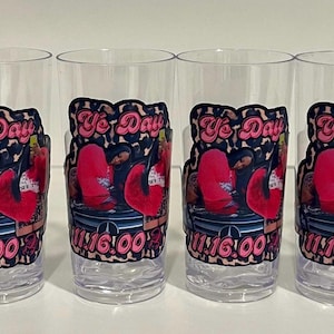 Pu&ograve; includere: Sei bicchieri in plastica trasparente disposti in fila, ognuno con una decalcomania grafica con il testo "Ye Day" e "11:16:00" in rosa, insieme a un'illustrazione stilizzata di una persona in abito rosso seduta su una superficie scura con bordo leopardato.