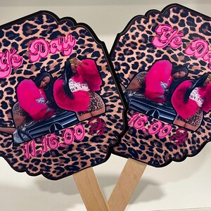May include: Two hand fans with a leopard print background. Each fan features a photo of two people wearing pink fur jackets. The fans have the text "Ye Day" and the date "11.16.00" in pink.
