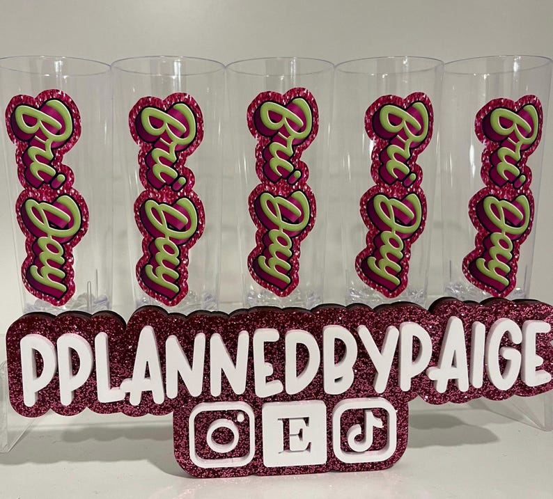 Pu&ograve; includere: Cinque bicchieri in plastica trasparente, ognuno con una decalcomania verticale con il testo Bri Day in lettere verde lime su sfondo magenta glitterato. Un cartello glitterato magenta mostra il testo bianco PPLANNEDBYPAIGE con icone.