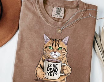 May include: A brown t-shirt with a cartoon cat holding a coffee mug that says "Is he dead yet?"