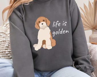 以下が含まれることがあります： チャコールグレーのスウェットシャツに、ゴールデン・ドゥードルの犬の漫画のイラストと「life is golden」の文字がプリントされています。