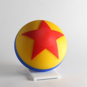 May include: A yellow, blue, and red toy ball with a red star on it. The ball is on a white stand.