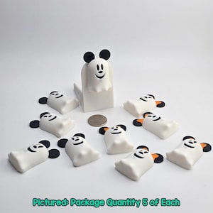 May include: A collection of white ghost-shaped figurines with black ears and smiling faces, along with a larger ghost figure. The text "Pictured: Package Quantity 5 of Each" is at the bottom. A coin is also present.