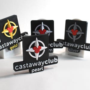 May include: Four black plastic keychains with a compass design and a Mickey Mouse head in the center. The keychains are labeled "Castaway Club" with the words "gold", "silver", and "pearl" underneath.