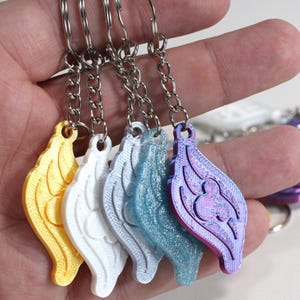 May include: Five keychains with different colored wings. The wings are yellow, white, light blue, and purple. Each keychain has a silver chain.