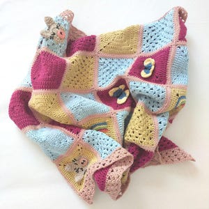 Peut inclure: Une couverture au crochet faite à la main, de conception patchwork. La couverture présente des carrés roses, jaunes et bleus, avec des appliqués décoratifs de papillons et d'animaux. Les bords sont finis avec une bordure festonnée.
