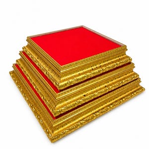 May include: A set of three square display risers stacked in a pyramid formation. Each riser features a metallic gold frame with an ornate, textured border and a flat, vibrant red velvet top surface. The square bases decrease in size from bottom to top.