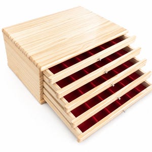 Op de afbeelding: Een opbergkist van lichtgekleurd hout met vier uitschuifbare lades. Elke lade is bekleed met een felrode fluwelen stof en verdeeld in meerdere kleine vierkante vakjes. De kist heeft een gladde afwerking met een natuurlijke houtnerf.
