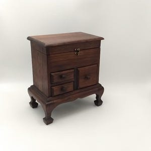 May include: A dark brown wooden jewelry box with a hinged lid and four drawers. The box is raised on four legs.