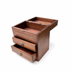 May include: A wooden jewelry box with a hinged top and three drawers. The box is made of dark brown wood and has brass-colored hardware. The drawers are partially open, revealing the interior.
