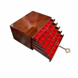 May include: A polished dark brown wooden jewellery chest featuring five tiered, pull-out drawers. Each drawer is lined with a vibrant red velvet interior, designed with multiple slots for organising items. A decorative brass key is inserted into the lock.