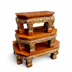 May include: Three wooden display stands stacked on top of each other. The stands are a rich brown color with ornate gold-colored accents. Each stand has a hexagonal top and decorative legs.
