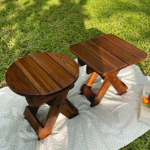 Puede incluir: Dos taburetes plegables de madera con un acabado marrón natural. Los taburetes están hechos de madera maciza y tienen un diseño simple y rústico. Son perfectos para agregar asientos adicionales a un patio o jardín.