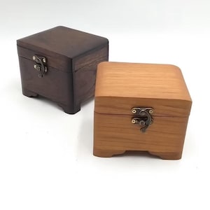 Puede incluir: Dos cajas de madera con tapas con bisagras y cierres de latón. Una caja es de color marrón oscuro y la otra es de madera clara.