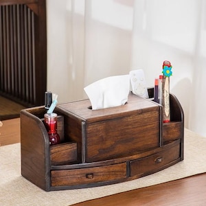 Op de afbeelding: Een donkerbruine houten bureau-organizer met twee laden, een tissueboxhouder en meerdere vakken om pennen, potloden en andere kleine items op te bergen.
