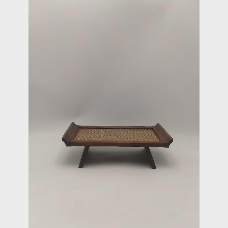 K&ouml;nnte beinhalten: Ein niedriger, rechteckiger Holztablett mit einer gewebten, hellbraunen Mitte. Das Tablett hat einen dunkelbraunen Rahmen und Beine. Das Design ist schlicht und elegant, geeignet zum Servieren oder Ausstellen.