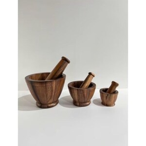 Könnte beinhalten: Drei Holz-Mörser- und Stößel-Sets in verschiedenen Größen. Die Mörser sind schalenförmig mit rundem Boden, und die Stößel haben einen zylindrischen Griff. Das Holz hat einen warmen, braunen Farbton. Die Sets sind auf einer weißen Oberfläche angeordnet.