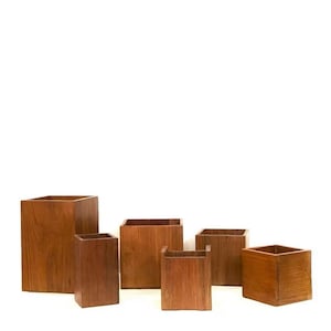 May include: A collection of six wooden square-shaped containers of varying sizes. The containers are made of a warm-toned wood, with visible grain patterns. The boxes are open at the top, suggesting they are designed for storage or display.