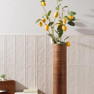 Op de afbeelding: Een hoge, gestreepte houten vaas met een tak van kunstmatige citroen takken met gele vruchten.
