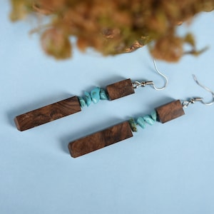 Puede incluir: Un par de pendientes largos de madera con piedras turquesa y ganchos de plata.