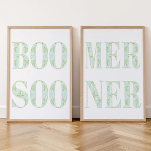 May include: Two vertical rectangular wall art prints in light wooden frames. The left print displays the letters BOO and SOO in a light green and blue floral pattern. The right print displays the letters MER and NER in the same matching pattern.
