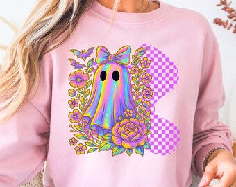 Può includere: Una felpa rosa chiaro con un design a fantasma colorato. Il fantasma ha un fiocco ed è circondato da fiori, pipistrelli e un motivo a scacchi. Il fantasma è un arcobaleno di colori.