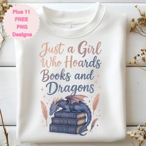 May include: White sweatshirt with the text "Just a Girl Who Hoards Books and Dragons." A blue dragon rests on a stack of books. The design includes feathers and stars.