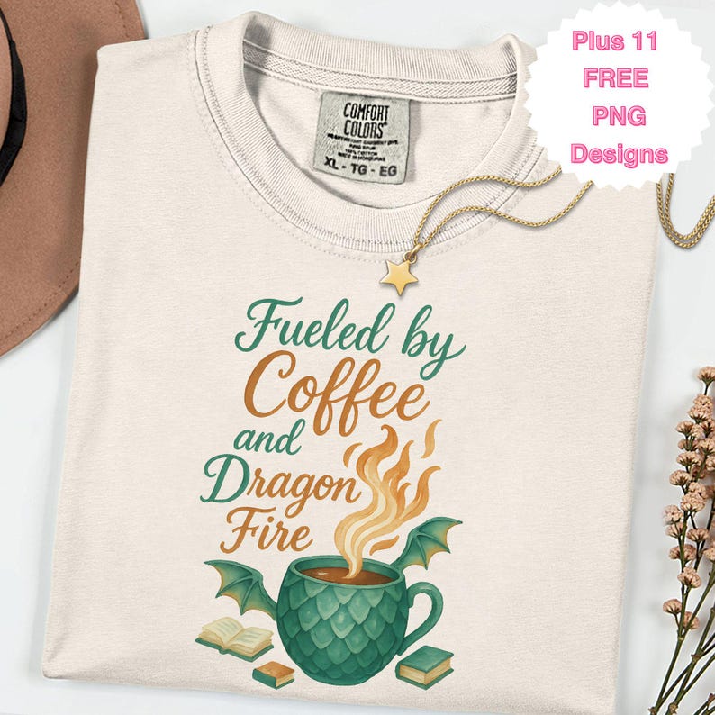 May include: Cream-colored t-shirt with the text "Fueled by Coffee and Dragon Fire" in green and orange. The design includes a coffee cup with dragon wings and flames. A gold star pendant necklace is draped on the shirt.