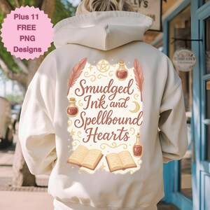 May include: Cream-colored hoodie with a graphic on the back that reads "Smudged Ink and Spellbound Hearts." The design includes feathers, potion bottles, books, and a crescent moon. A pink circle in the upper left corner says "Plus 11 FREE PNG Designs."