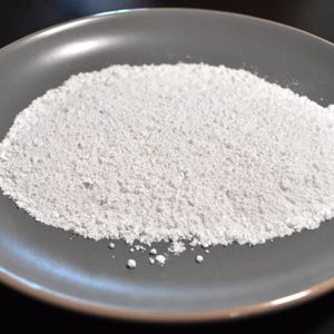 May include: A close-up of a white powder on a gray plate. The powder is fine and smooth, and it appears to be evenly distributed on the plate.