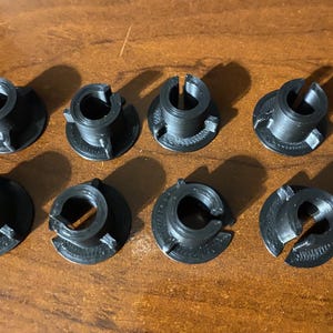 May include: Eight black plastic connectors with a center hole and a split on one side. The connectors are arranged in two rows of four.