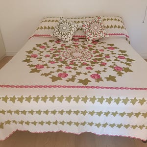 Può includere: Un copriletto bianco con un motivo floreale rosa e verde. Il copriletto ha un bordo bianco con un design floreale rosa e verde. Il copriletto è su un letto con due cuscini bianchi con un design floreale verde e bianco.