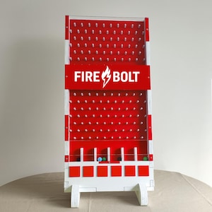 May include: A red and white wooden game with a pegboard design. The game features the text "FIRE BOLT" in white on a red banner. Several colored balls are visible at the bottom. The game is designed to stand upright on a table.